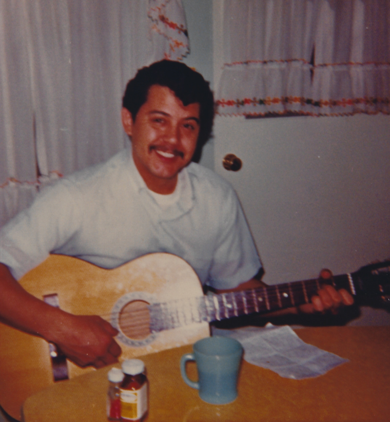 Eddie Gonzales smiling while playing an acoustic guitar