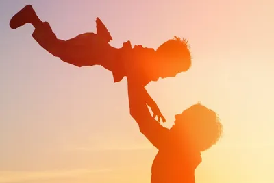 Silhouetted parent lifting a child against a warm sunset sky