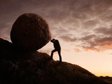 Silhouette pushing a huge boulder uphill at sunset