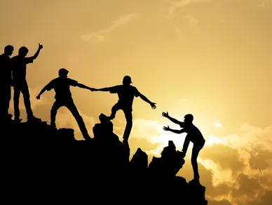Silhouetted group helping one another on a ridge at sunset for the Umbrella Ministries section