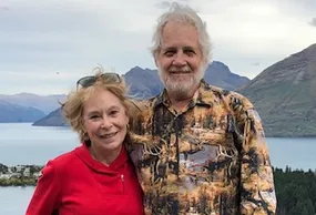 Margie and Chris Johnson standing outdoors with mountains and water in the background