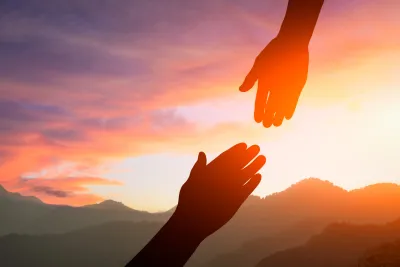 Two hands reaching toward each other at sunset, symbolizing support and connection