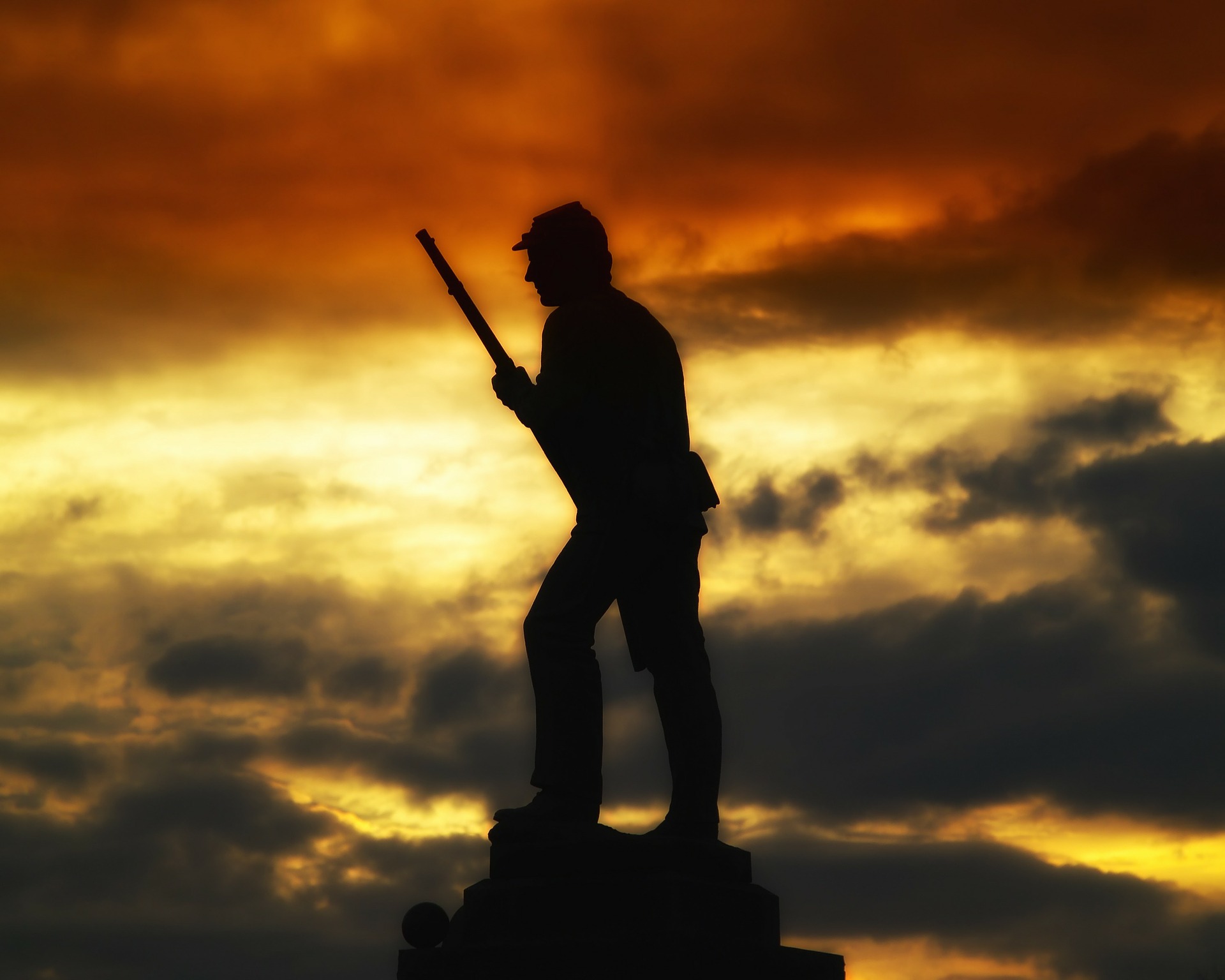 Silhouette of a soldier statue against a dramatic sunset sky
