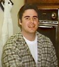 Portrait of a person seated indoors in a plaid overshirt