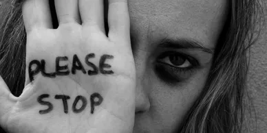 Woman holding up a hand with the words Please Stop written on it
